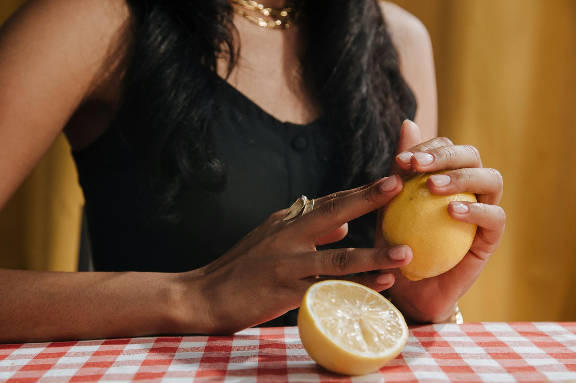 A hand holding a fresh lemon at a dining table against a warm background.