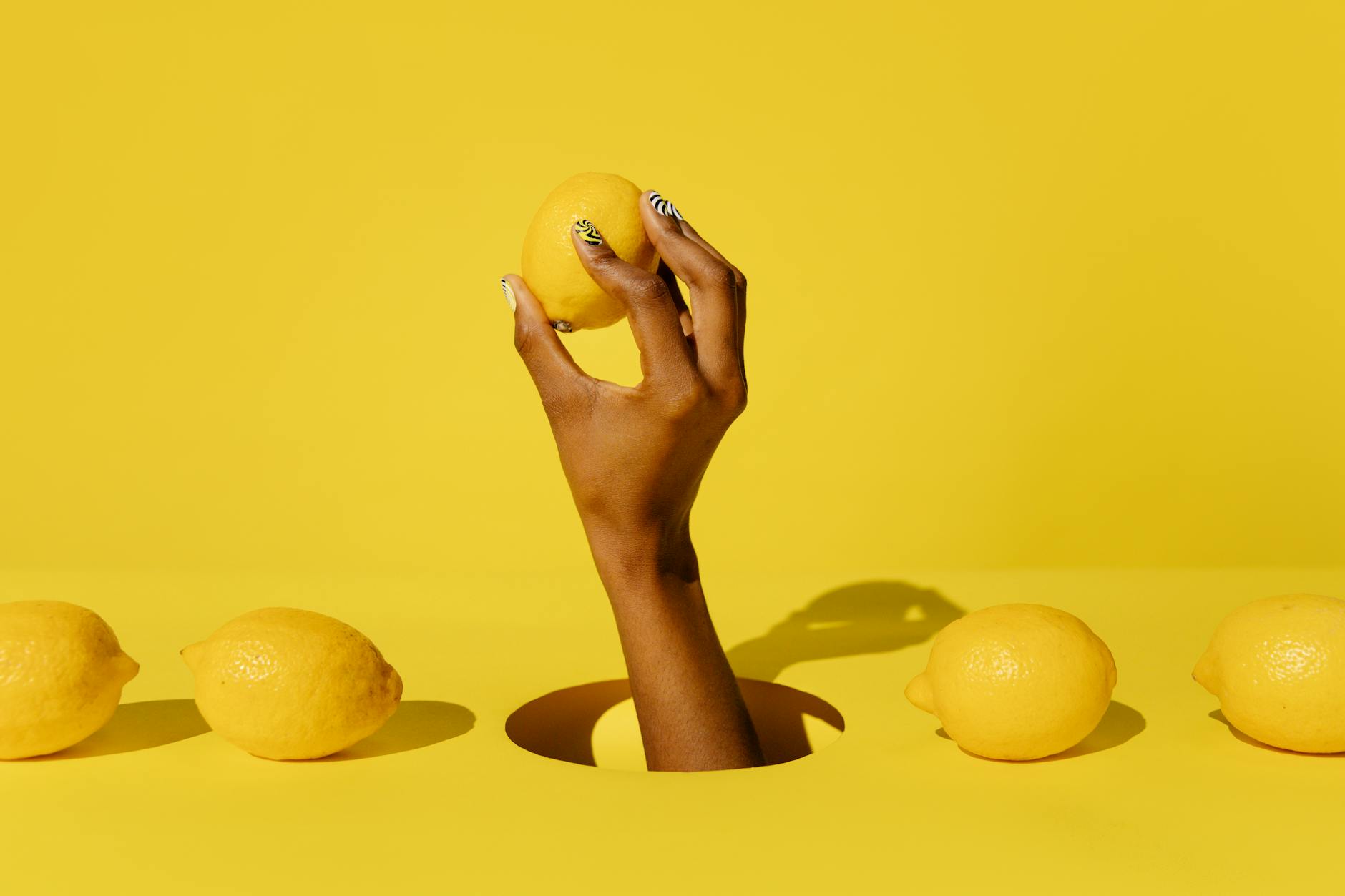 A hand holding a fresh lemon against a vivid yellow background, symbolizing renewal and starting fresh
