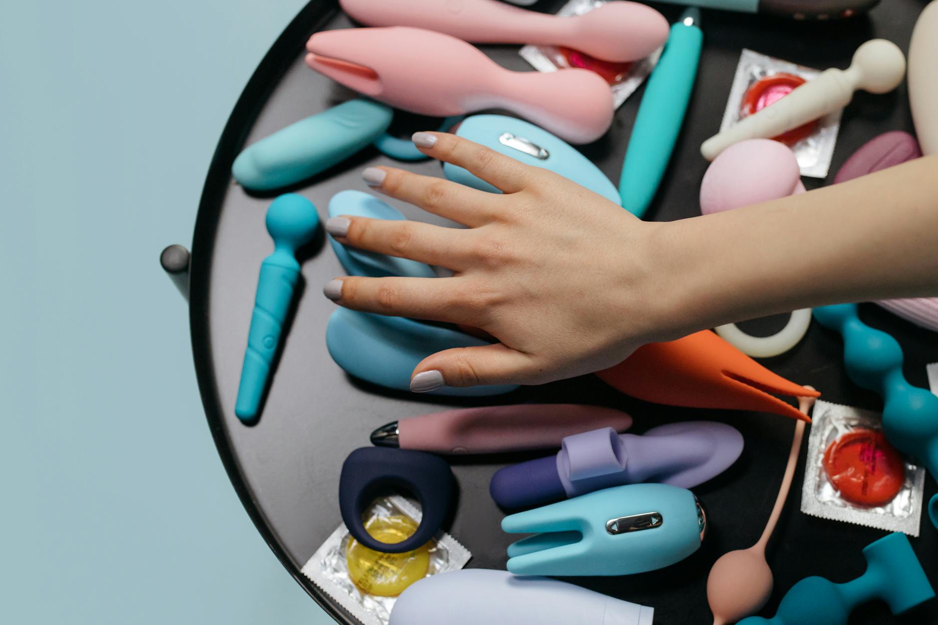 Mão alcançando uma coleção de vibradores coloridos, simbolizando escolha e exploração segura