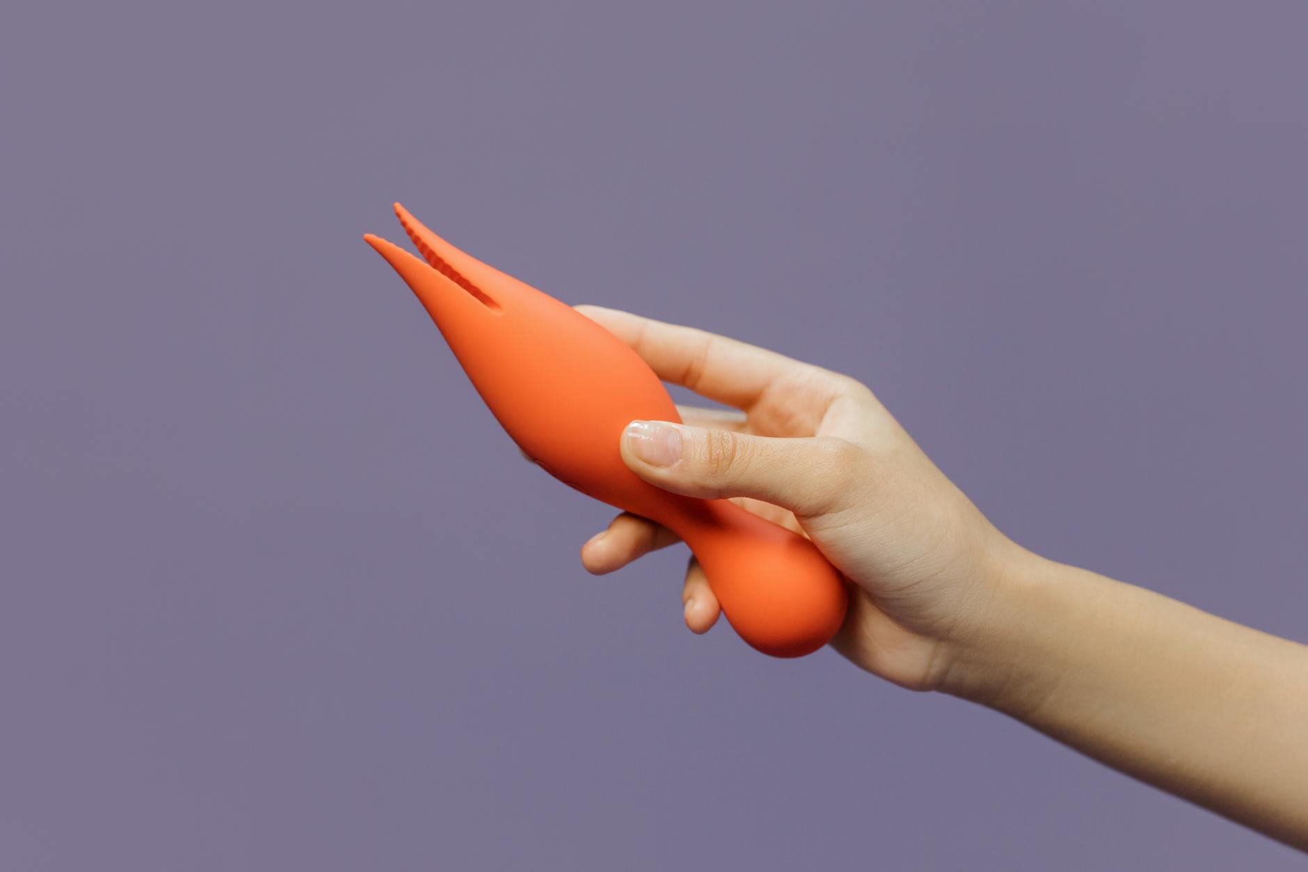 Close-up of a hand holding a bright yellow vibrator against a minimalistic purple backdrop, showcasing modern intimacy