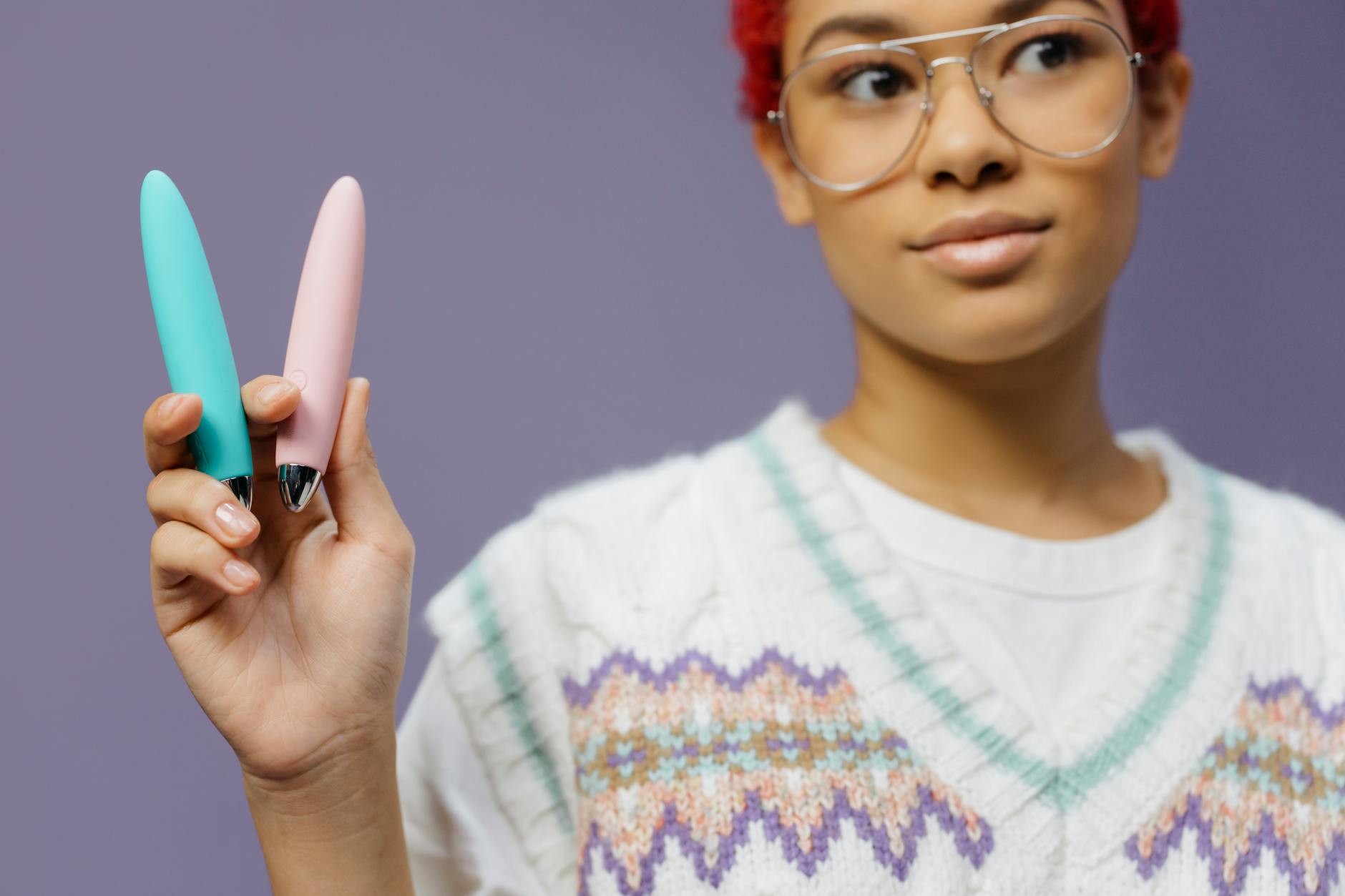 Close-up of hands holding a sleek blue vibrator against a purple background, representing intimate pleasure and connection