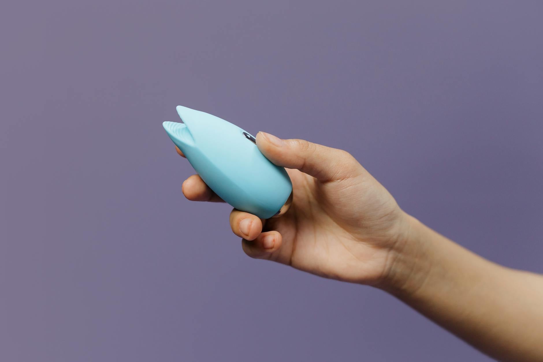 A vibrant blue silicone clitoral vibrator held in hand, demonstrating the lemon sexual toy design against a purple background.