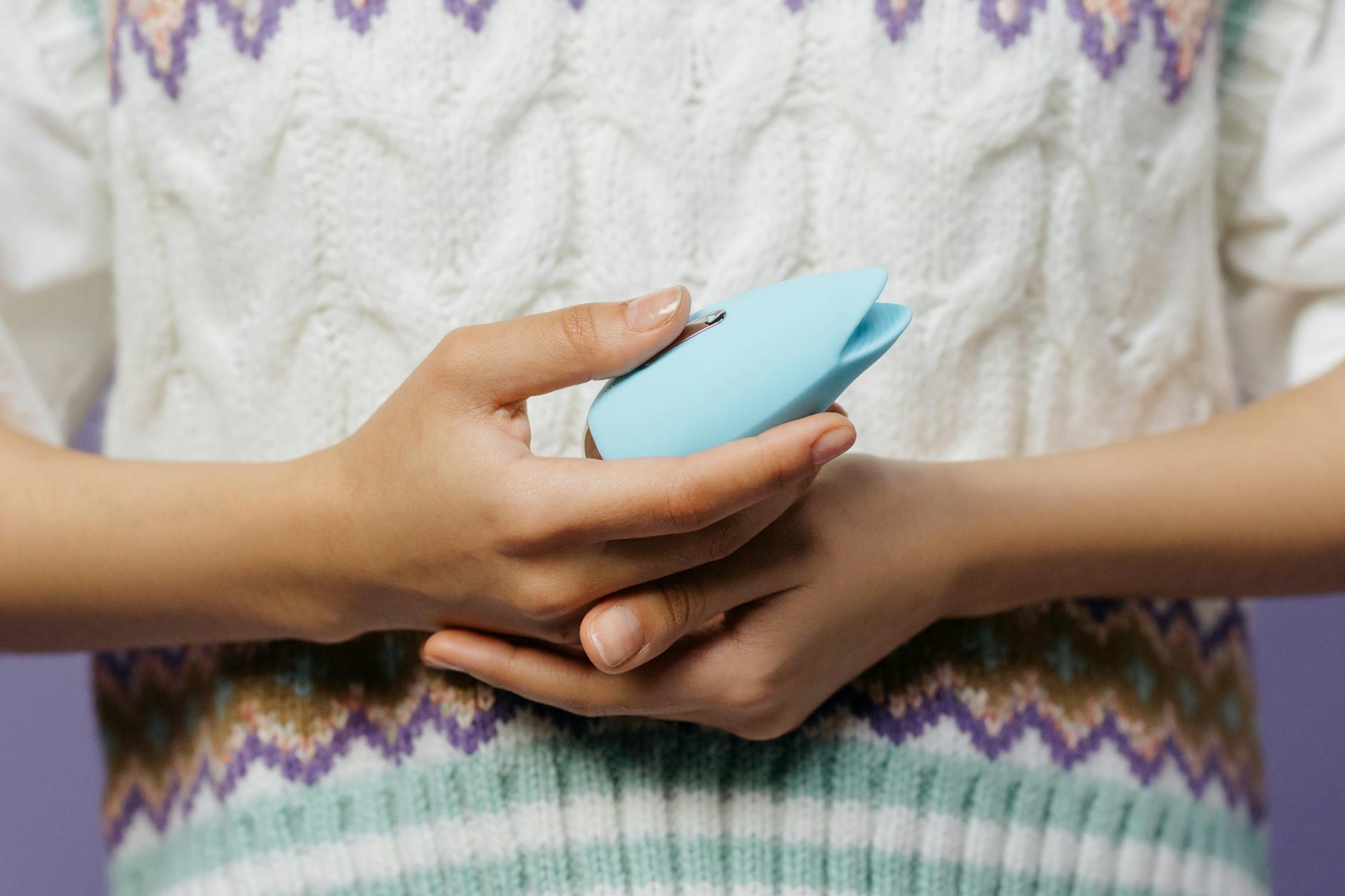 Hand reaching over a collection of colorful clitoral vibrators arranged on a table.