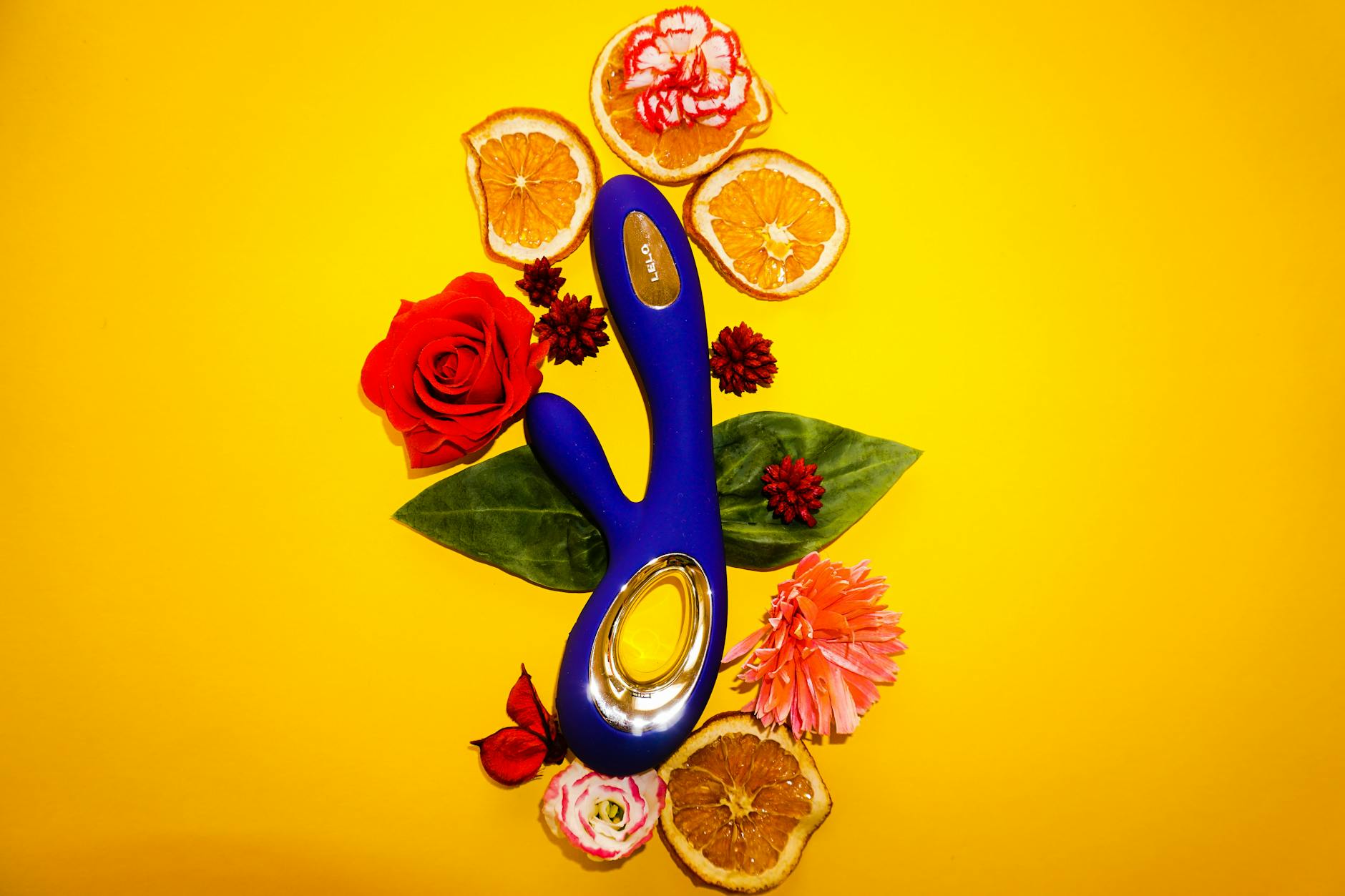 A blue vibrator surrounded by fresh lemons and orange slices on a bright yellow background